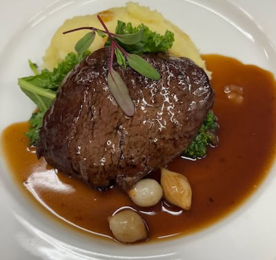 Gourmet beef tenderloin with mashed potatoes and vegetable garnish on a white plate.