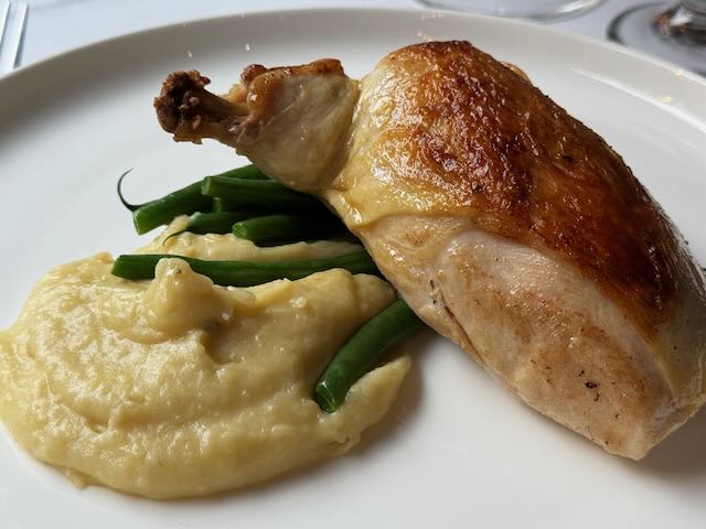 Roasted chicken leg with green beans and mashed potatoes on a white plate.