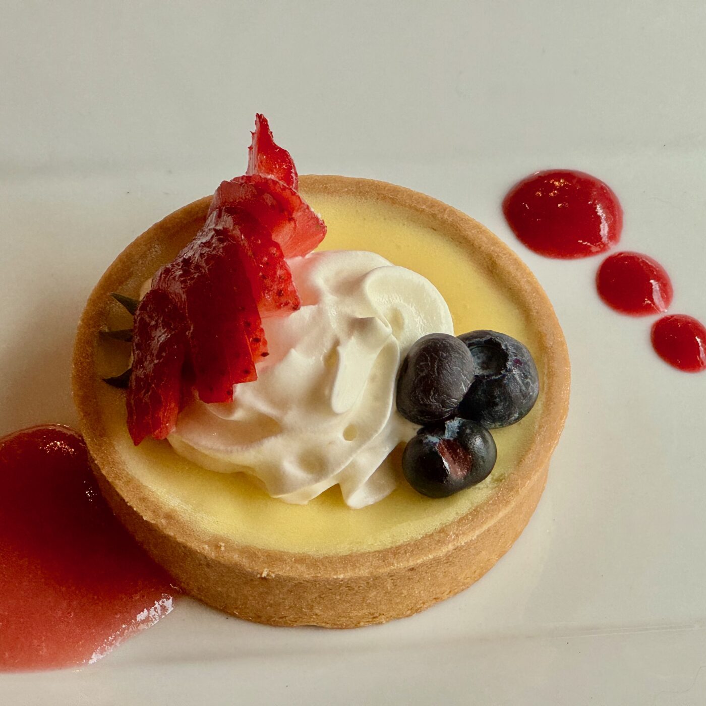 Fruit tart with strawberries, blueberries, and whipped cream on a white plate.