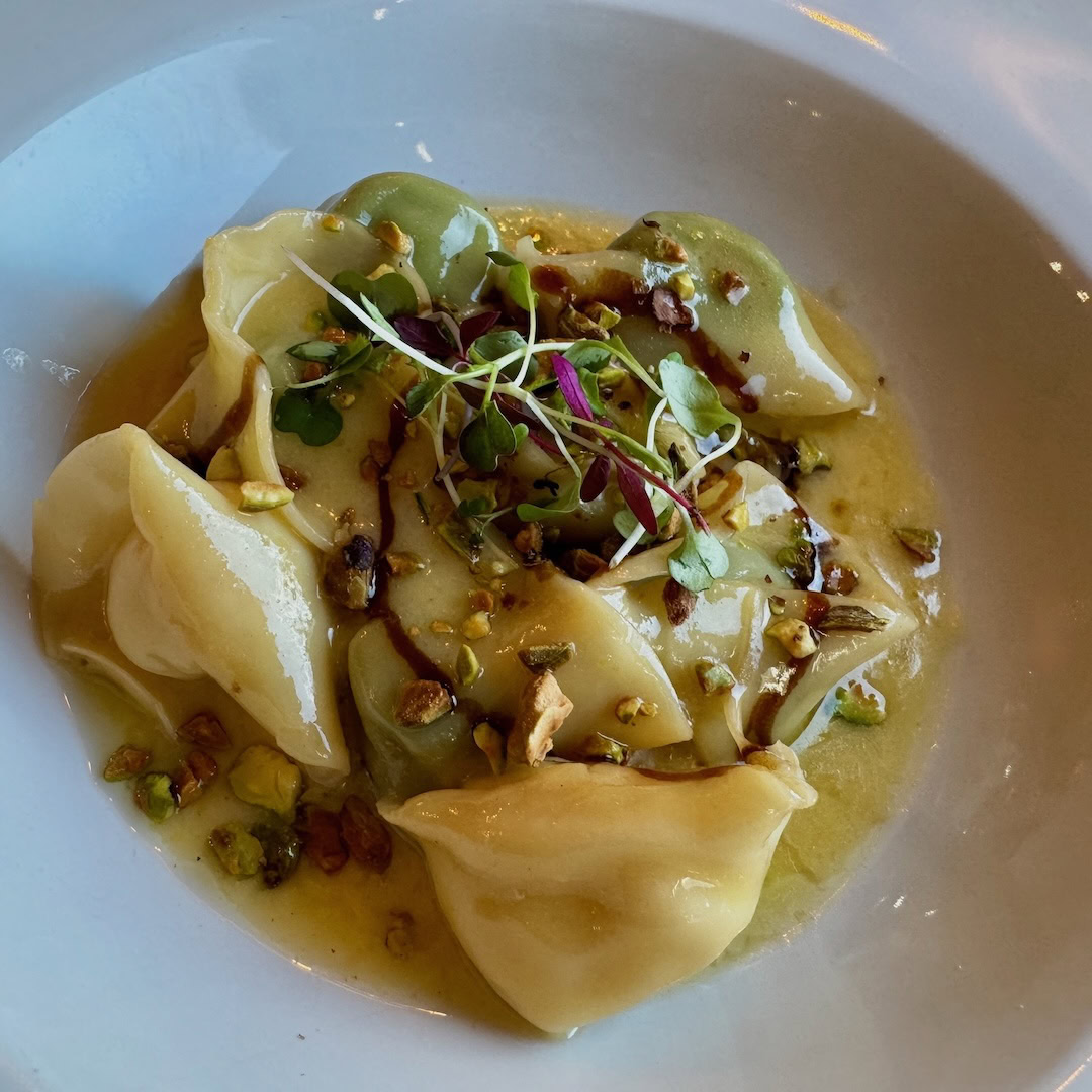 Delicious ravioli with microgreens and chopped nuts on a white plate.