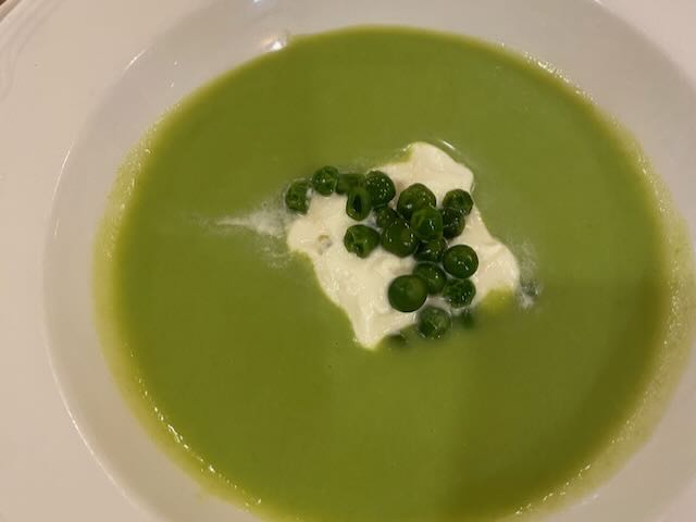 Green pea soup with cream and green peas on top, served in a white bowl.