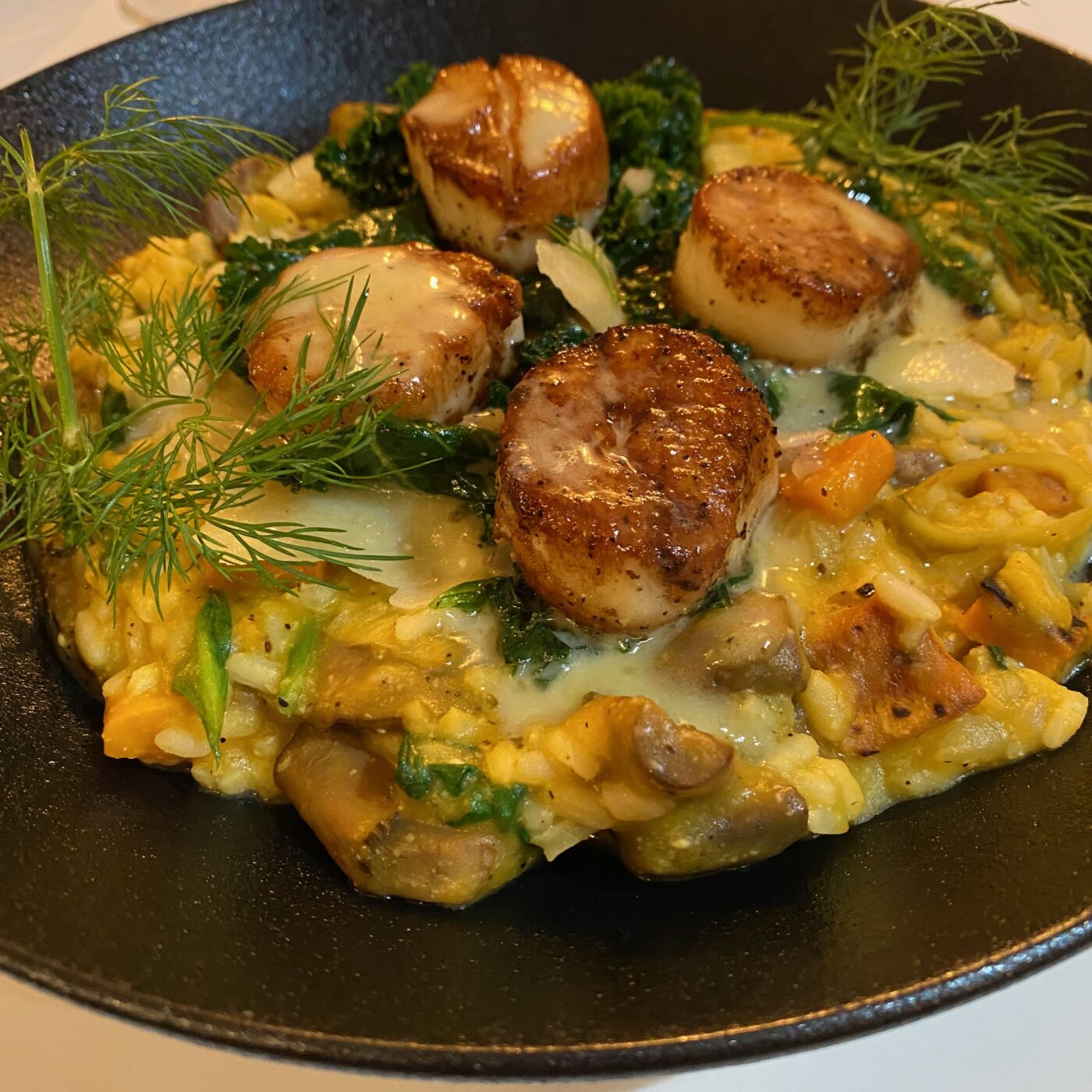 Seared scallops with vegetables and herbs on a black plate at Strewn Winery.
