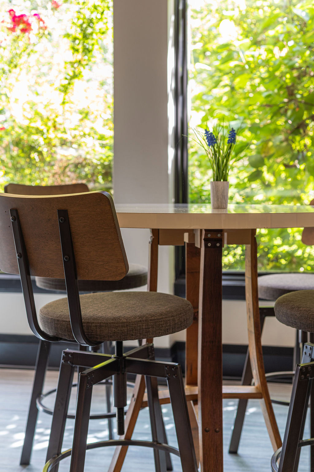 Cozy winery interior with wooden chairs and a table near large windows showing green foliage outside.
