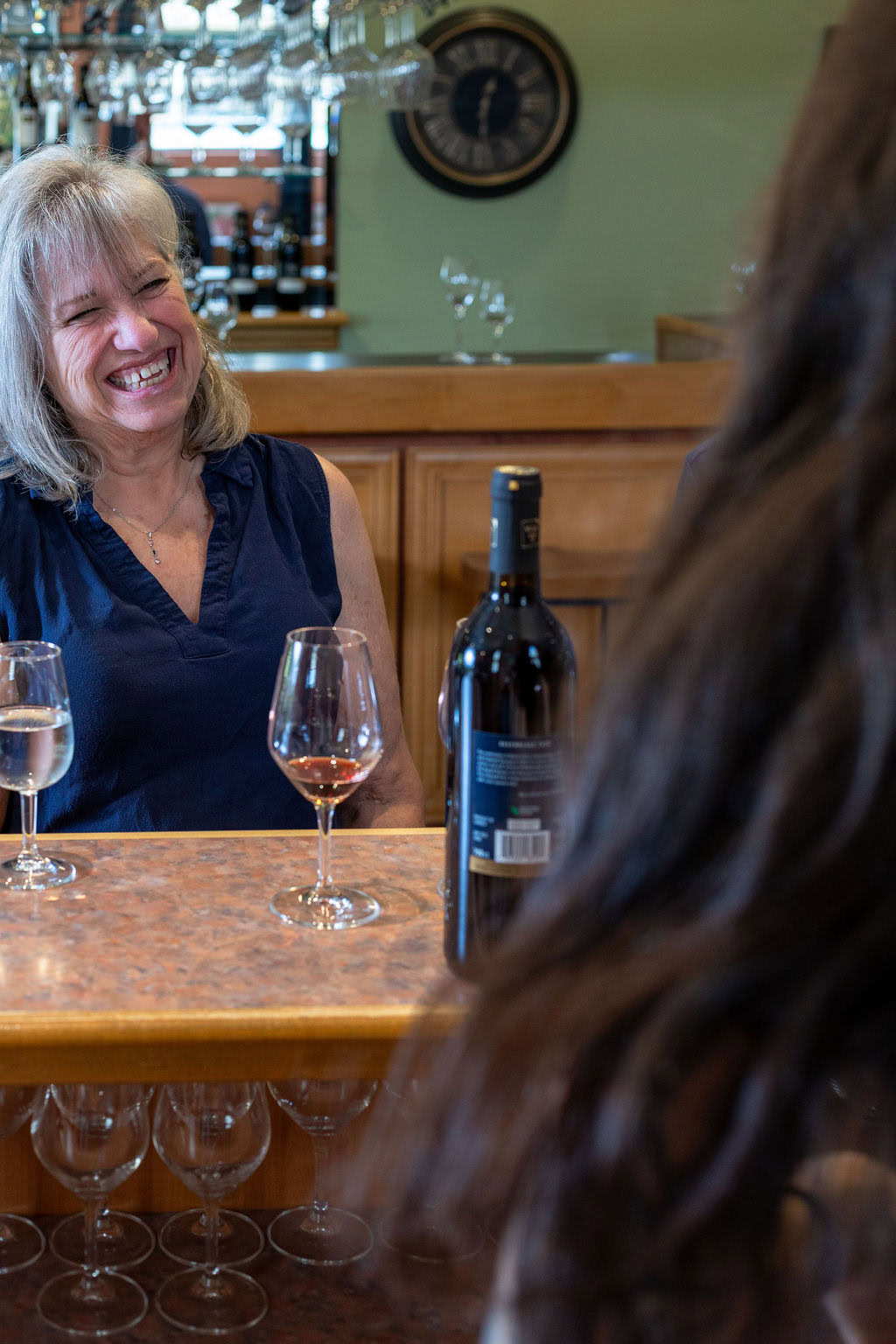 Smiling woman enjoying wine tasting at Strewn Winery with glasses and wine bottle on the table.